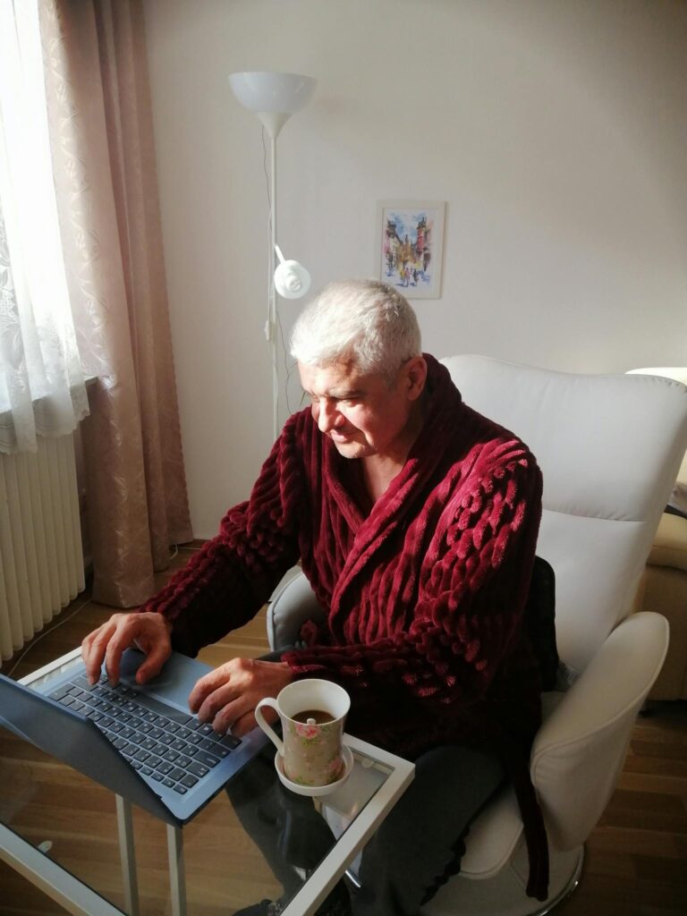 High angle of serious aged man in bathrobe having coffee while working remotely at home