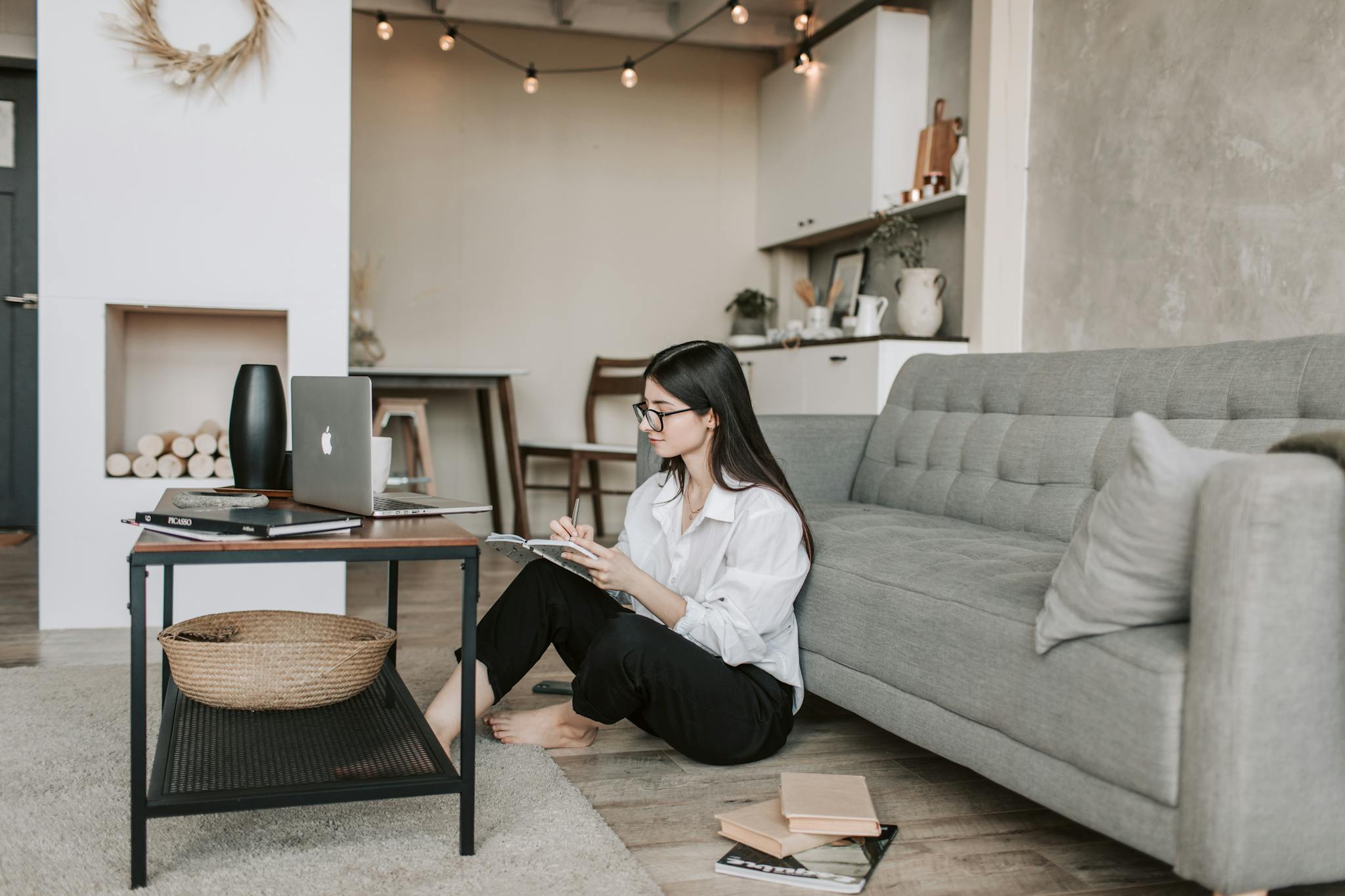 Woman working remotely from a cozy home office, seated on the floor with laptop and notebook.